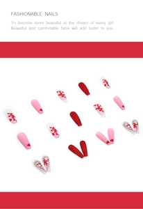 Detailed flat lay of long ballet press-on nails with red heart patterns and rhinestone accents