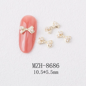 Close-up of 10.5x5.5mm bow nail art charms with golden alloy base and white pearls