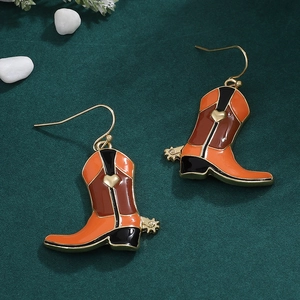 Macro shot of orange and brown enamel western cowboy boot drop earrings on a green surface