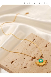 Detail of gold evil eye pendant with turquoise enamel and textured fan-shaped edge