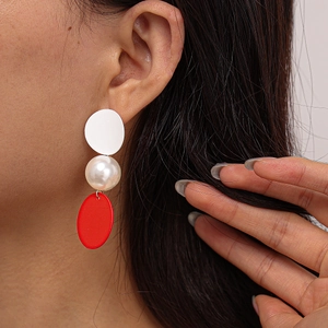 Close-up of asymmetric red and white geometric earrings with faux pearl on ear