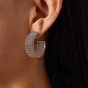 Close-up of silver-tone hollow bead woven C-shaped earrings on model ear with metallic texture