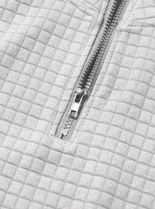 Close-up of high-quality metal zipper and quilted grid texture on light grey sweatshirt