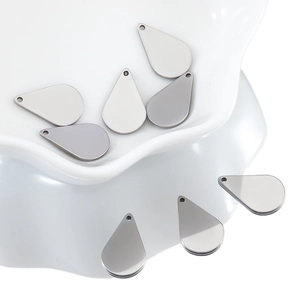 Polished silver stainless steel water drop pendants displayed on a white ceramic tray