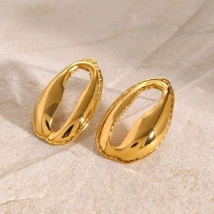 Detail of 18k gold hollow oval earrings with textured edges on a beige stone base