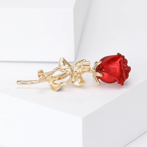 Elegant gold-tone rose brooch with vibrant red petals on a white geometric background