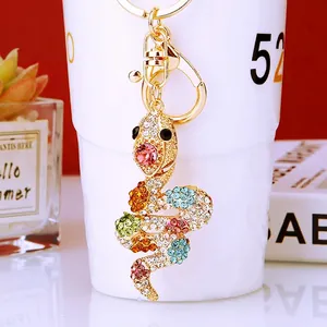 Golden snake keychain pendant with colorful rhinestones on a white porcelain cup background