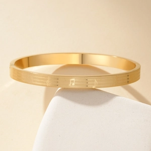 Gold stainless steel musical note engraved bangle displayed on a minimalist stone pedestal