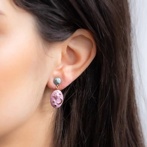 Detail of asymmetrical star and moon enamel stud earrings worn on model's ear