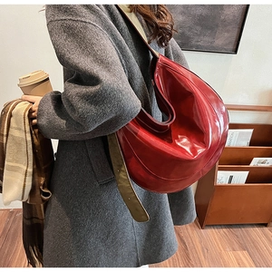 Close-up of a large red glossy PU leather crescent shoulder bag worn with a wool coat