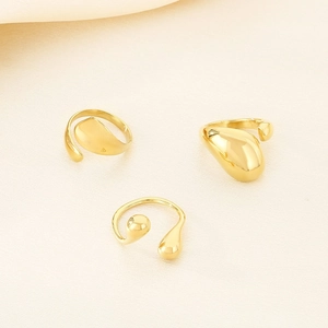 Detailed view of three 18K gold-plated irregular fluid rings on beige fabric texture