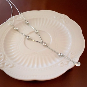Detail of silver Y-shaped long necklace with crystal pavé on baroque ceramic plate