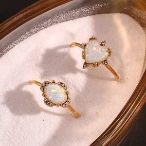 Close-up of heart and oval opal rings in gold finish resting on white sand detail