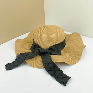 Detail of wide brim straw sun hat featuring elegant black pleated ribbon bow decoration