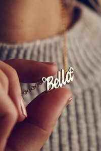 Close-up of gold-plated Mama necklace featuring custom Bella name pendant on gray sweater