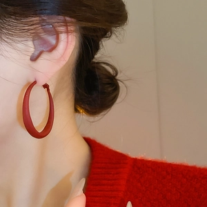 Close-up of a model wearing large matte red C-shaped hoop earrings with a textured finish