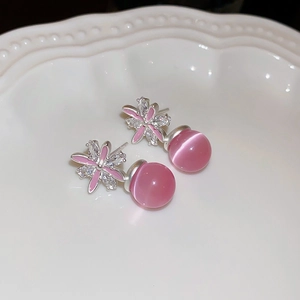 Detailed close-up of pink flower earrings with zircon and cat eye stone on a ceramic tray
