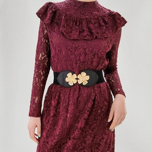 Detail of a black elastic waist belt featuring a decorative golden flower buckle on a dress