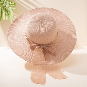 Detail of pink wide brim straw hat with elegant ribbon bow and pearl decorations