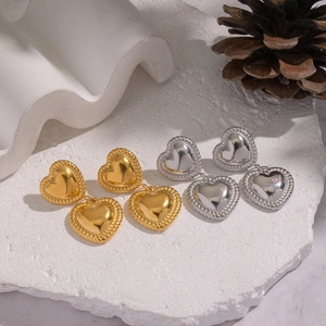 Artistic gold and silver heart-shaped stainless steel earrings on white stone base
