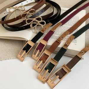 Close-up of assorted thin leather belts with gold bow and square buckles on a rustic background