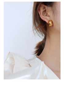 Macro view of gold twisted metal earrings with polished 18K finish on a model