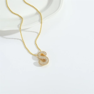 Close-up of golden bubble letter S pendant necklace with sparkling stone inlay
