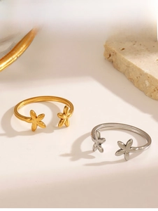 Close-up of gold and silver flower open rings on a neutral textured stone surface