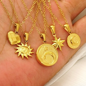 Gold plated stainless steel sun and moon pendant necklaces held in hand for display