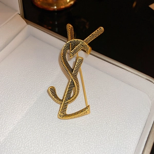 Close-up of golden vintage YSL logo brooch displayed in a luxury white jewelry box