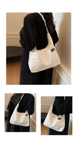 Detail of a minimalist white canvas shoulder bag with a brown leather fashion logo patch