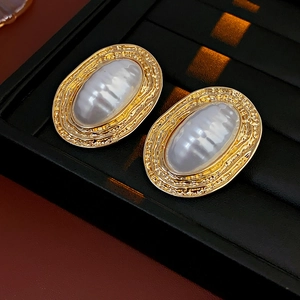 Detail view of gold textured oval earrings with white pearl-like inlay on a jewelry tray