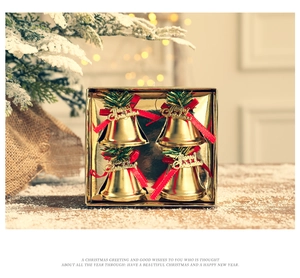 Golden Christmas bell ornaments with red bows and pine needles in a festive gift box