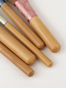 Detail of 5 mini makeup brushes with natural wood handles and floral patterned metal ferrules