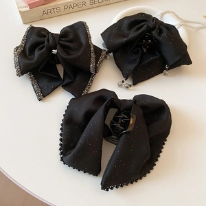 Detailed view of black satin bow hair claws with sparkling rhinestones and pearl accents
