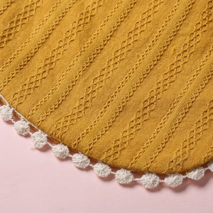 Détail macro du bavoir en tricot jaune gingembre avec motif losange et bordure dentelle