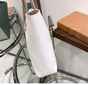 Side view of white tote bag with brown straps and golden rivets detailing texture
