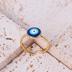 Close-up of golden evil eye ring with blue enamel inlay on a beige stone surface