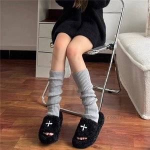 Gray ribbed knit leg warmers paired with black plush slippers in a cozy home setting