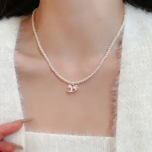 Elegant pearl necklace with a pink enamel horse pendant worn on a white cardigan