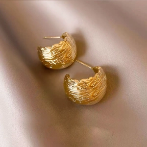 Minimalist golden C-shape geometric earrings with hammer texture on silk background