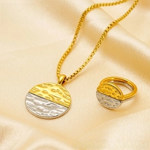 Macro shot of gold and silver dual-tone hammered pendant necklace and ring on silk fabric