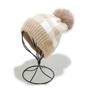 Detail of knit beanie with beige checkerboard pattern and fluffy faux fur pompom