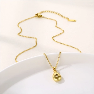 Gold stainless steel teardrop necklace with star pattern and zircon on a ceramic tray