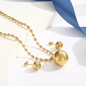 Close-up of a minimalist golden ball necklace and earring set on white geometric props