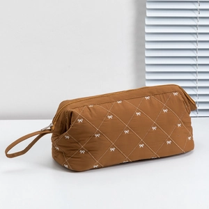 Close-up of brown quilted toiletry bag with white bow embroidery and side handle strap