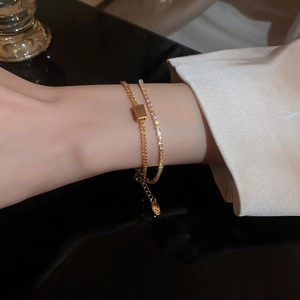 Detailed view of double-layered gold-plated bracelet with zircon square charm on wrist