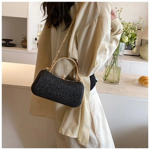 Detail of black glitter evening bag with gold frame and chain strap on a model