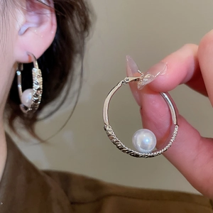 Detailed close-up of silver hoop earrings with spiral texture and white round pearls
