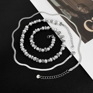 Detailed macro view of silver stainless steel snake chain and pearl necklace set on magazine